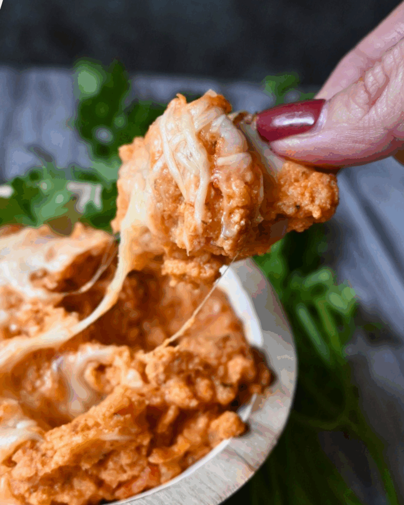 cheesy chicken parm dip on a cracker being held over a bowl full of the same