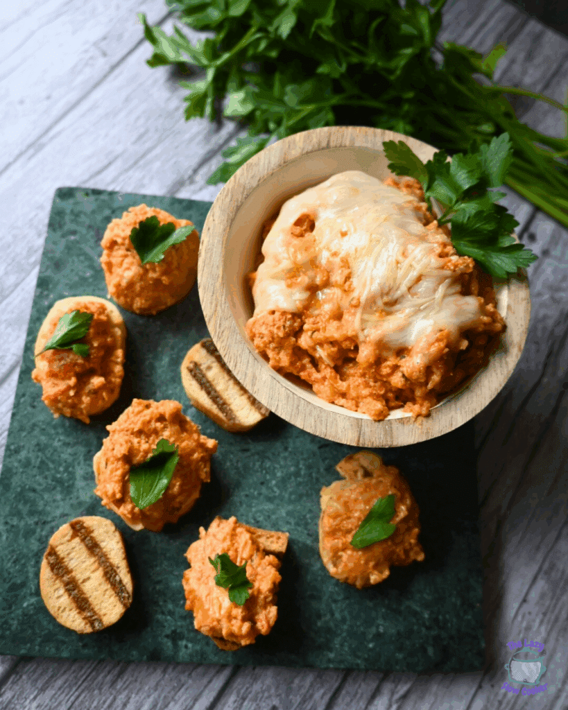 a bowl of slow cooker chicken parmesan dip with a few crackers and breadsticks
