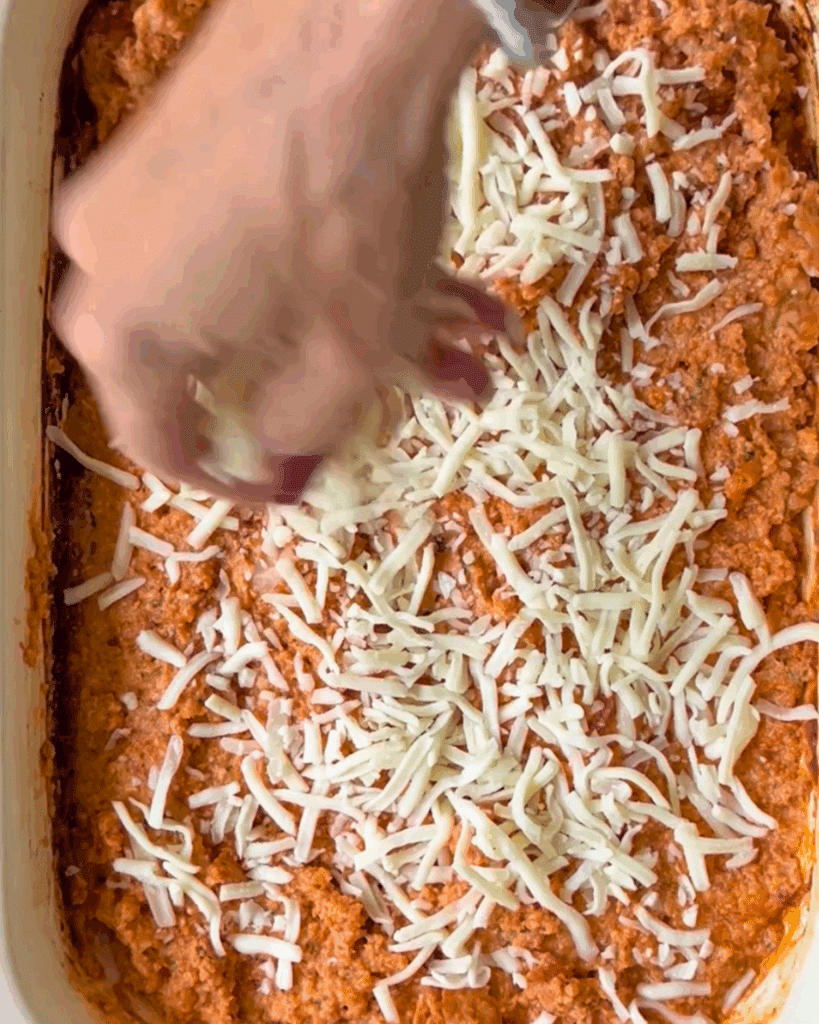 adding more cheese topping to a slow cooker filled with cooked cheesy chicken dip