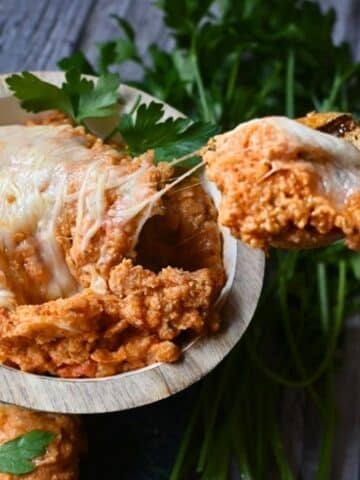 cheesy chicken parm dip on a cracker being held over a bowl full of the same