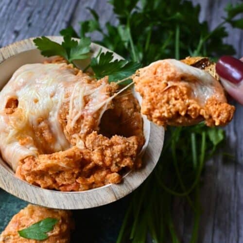 cheesy chicken parm dip on a cracker being held over a bowl full of the same