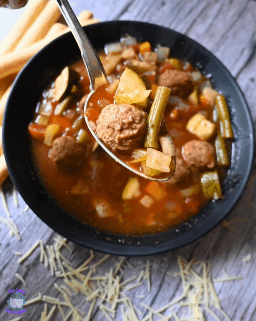 a spoonful of vegetable soup with meatballs made in a slow cooker held over a bowlful of the same