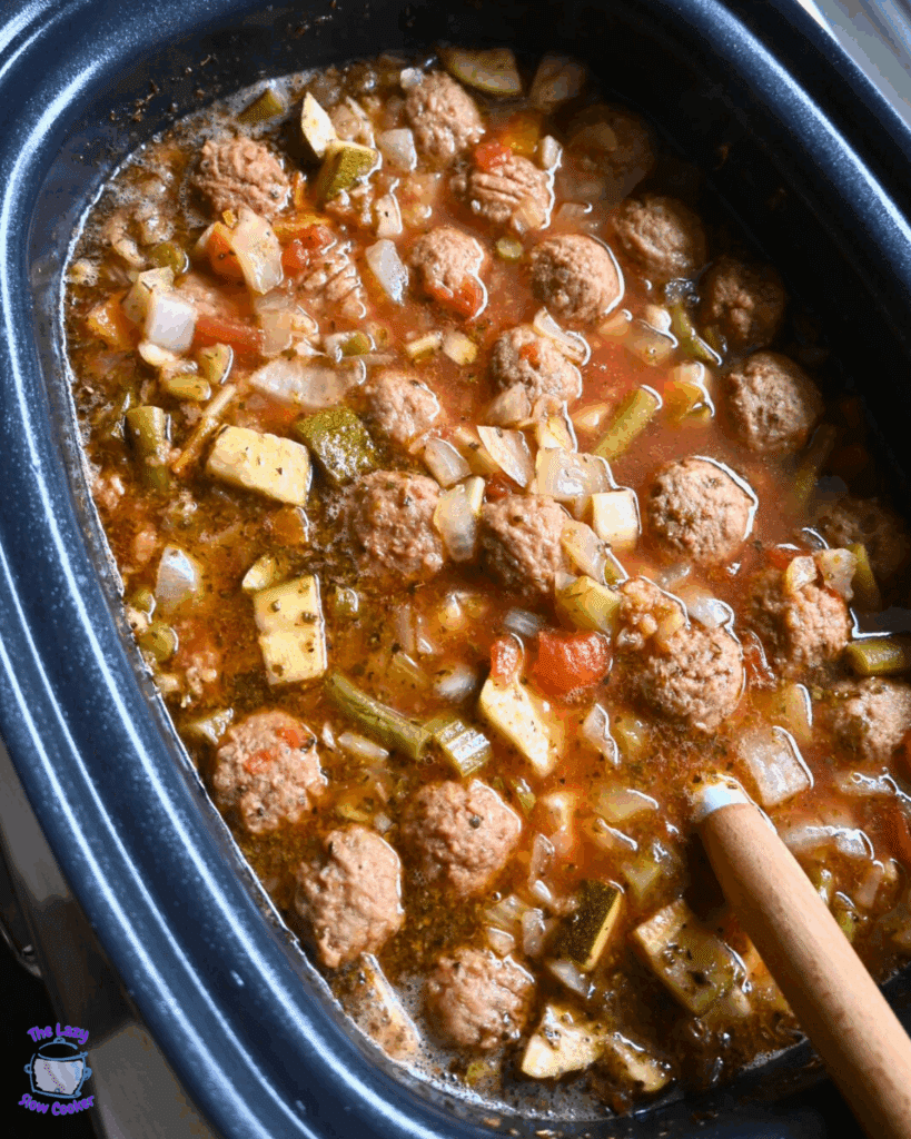 a slow cooker filled with vegetable meatball soup that is ready to serve