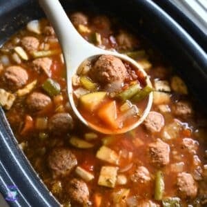 A ladle full of meatball vegetable soup held over a crockpot full of the same