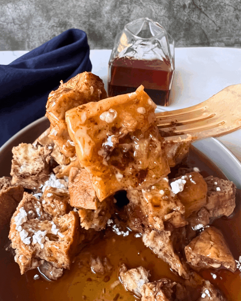 a cube of slow cooker french toast casserole on a fork dripping with syrup