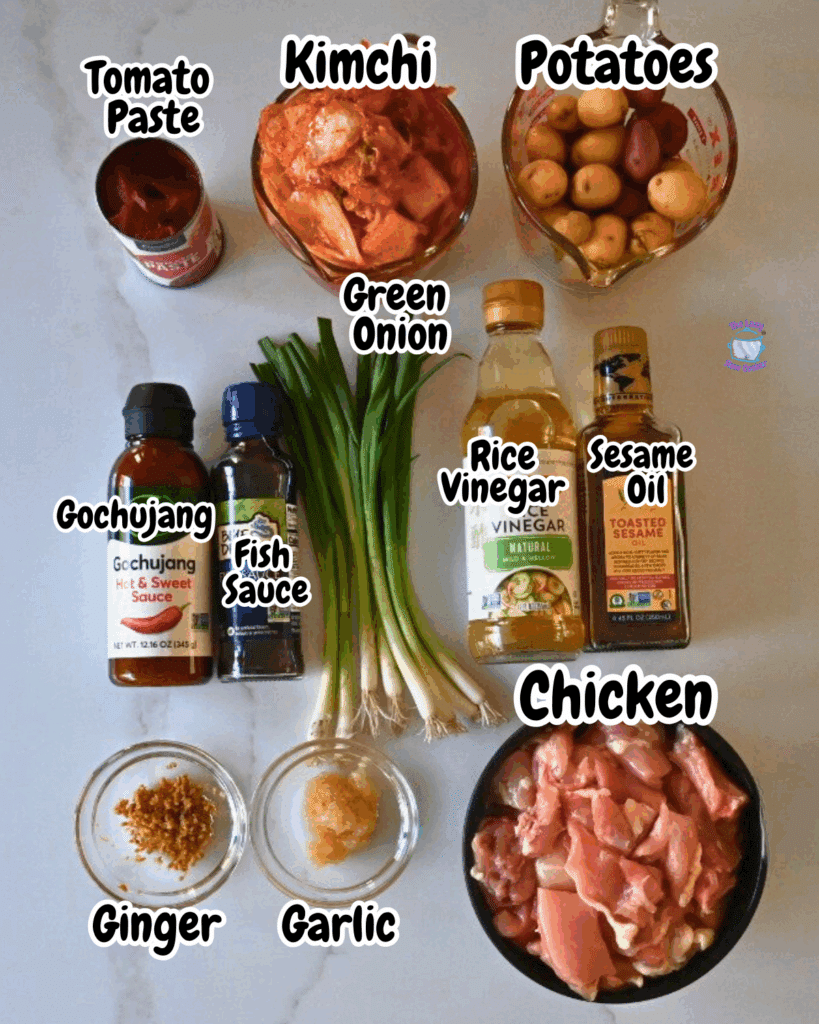 A top-down view of ingredients for a Korean dish on a table: tomato paste, kimchi, potatoes, green onions, gochujang, fish sauce, rice vinegar, sesame oil, chopped chicken, minced ginger, and garlic. Each item is labeled.