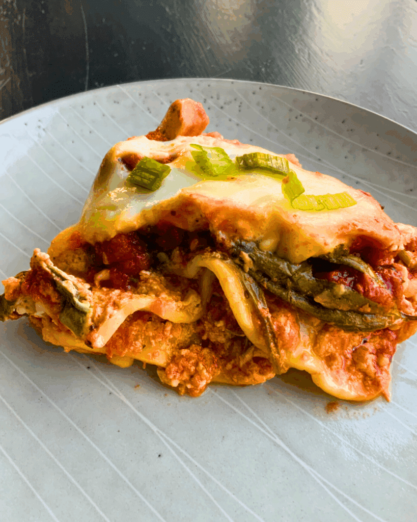 A slice of mushroom and spinach lasagna on a white plate topped with some chopped basil.