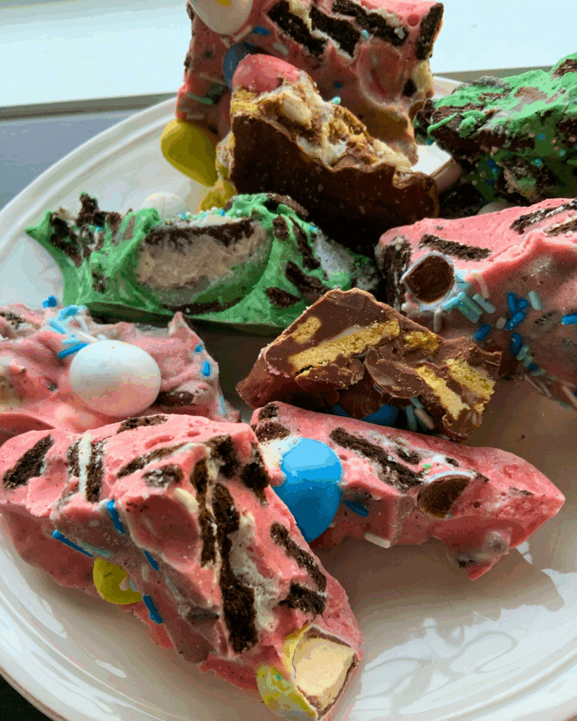 A plate with colorful, chunky pieces of dessert bark featuring pink and green swirled chocolate, chocolate cookies, candy-coated chocolate Easter eggs.