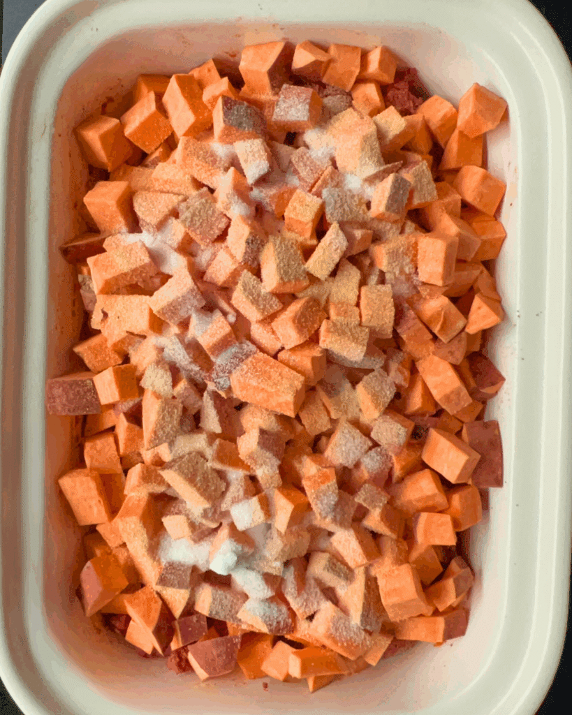 A casserole style slow cooker dish filled with diced sweet potatoes, sprinkled with salt and spices, ready to be cooked.
