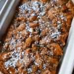 A slow cooker casserole dish filled with golden-brown bread pudding, topped with a generous dusting of powdered sugar.