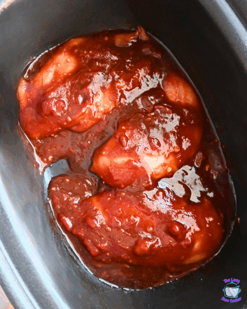 Raw chicken breasts coated in a thick honey garlic sauce inside a black slow cooker, ready to be cooked.