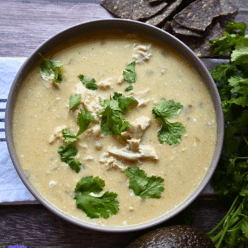 A bowl of creamy enchilada chicken soup topped with fresh chopped cilantro. The black bowl sits on a white cloth with dark stripes.