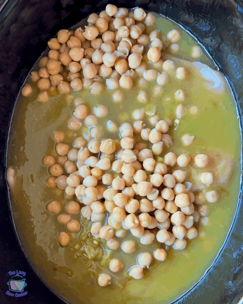 Chickpeas in a yellowish soup, inside a slow cooker. The chickpeas are spread across the surface, partially submerged in the liquid.