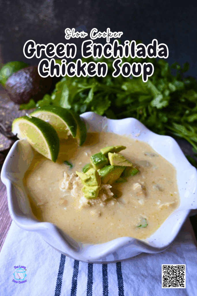 A bowl of creamy green enchilada chicken soup topped with avocado and lime wedges sits on a white napkin, with fresh cilantro and an avocado in the background. Text on the image reads, Slow Cooker Green Enchilada Chicken Soup