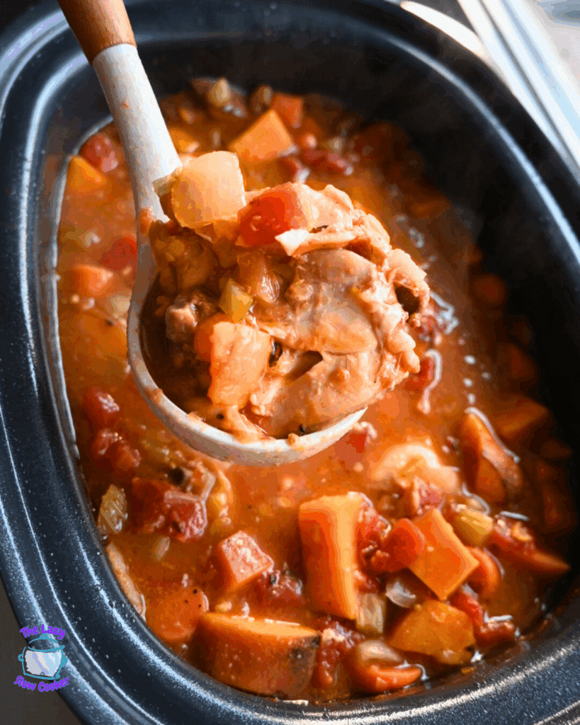 A ladle scoops up a hearty stew with chunks of meat, carrots, potatoes, and onions from a slow cooker filled with a rich, tomato-based broth.