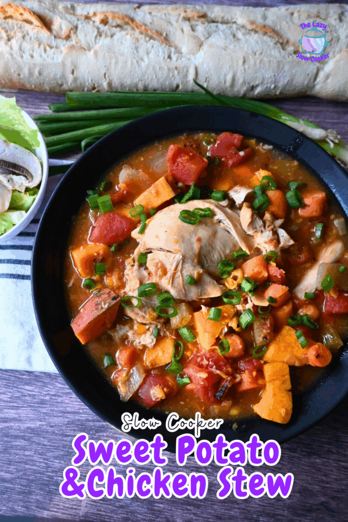 A bowl of chicken stew with sweet potatoes, tomatoes, and green onions, garnished with chopped green onions. A baguette, lettuce, mushrooms, and green onions are in the background on a wooden surface.