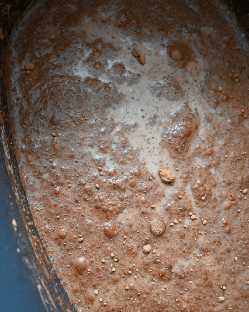 Close-up of chocolate batter in a bowl, showing bubbles, cocoa clumps, and an uneven surface before slow cooking