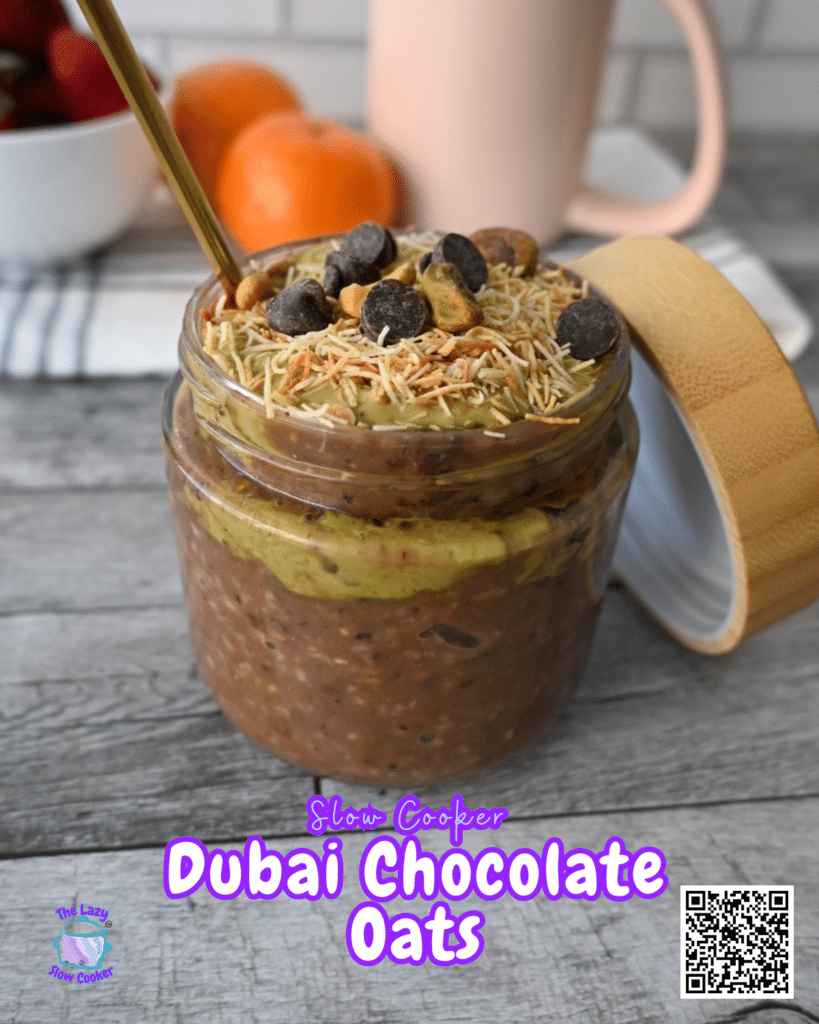 A jar with chocolate oats, pistachio butter, toasted kataifi and chocolate chips sits with a gold spoon. Text reads "Slow Cooker Dubai Chocolate Oats." Fruit and a QR code are in the background.