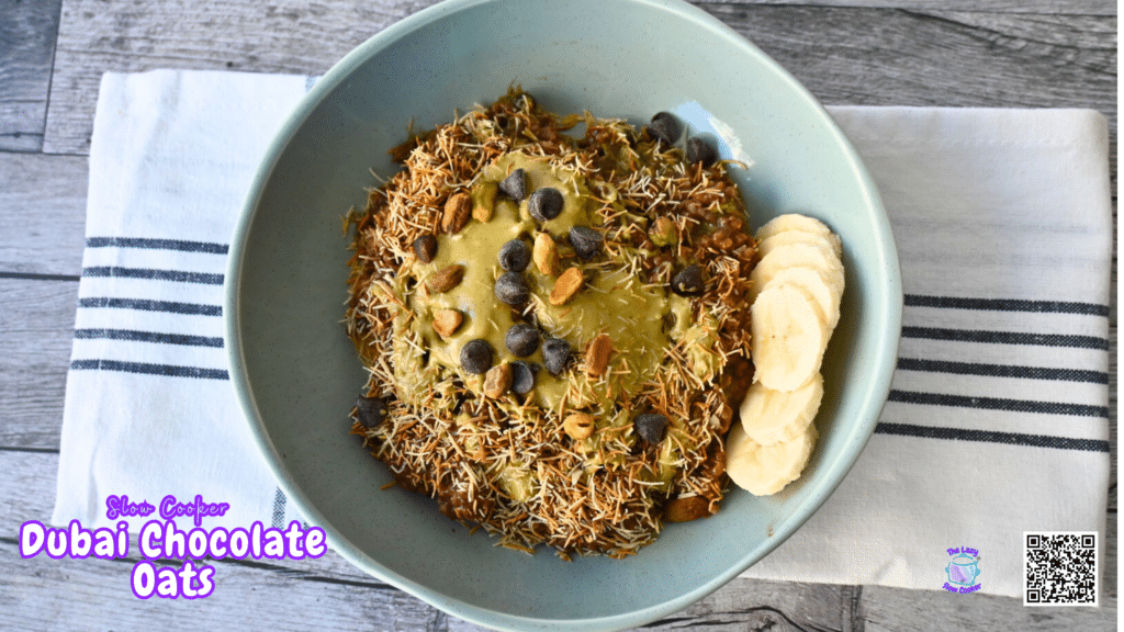 A blue bowl of oatmeal with kataifi, chocolate chips, nuts, nut butter, and banana slices on a striped cloth atop a wood table.
