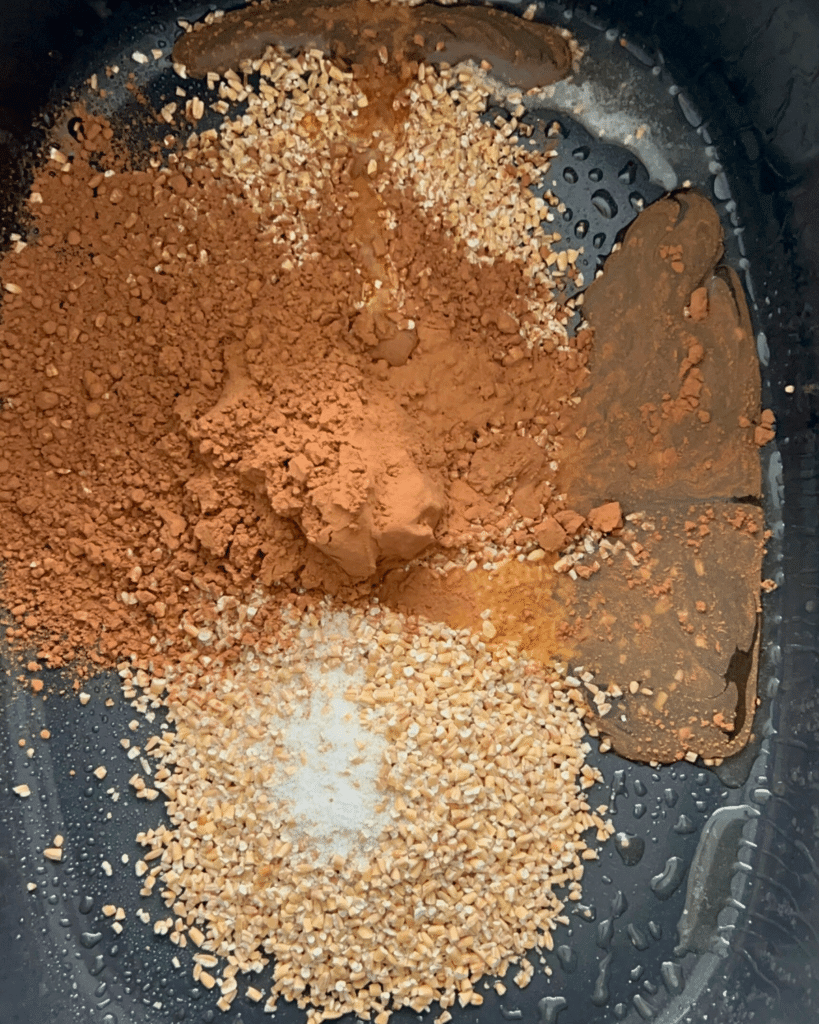 Close-up of a black slow cooker with steel-cut oats, cocoa powder, and salt ready to make Dubai chocolate slow cooker oatmeal