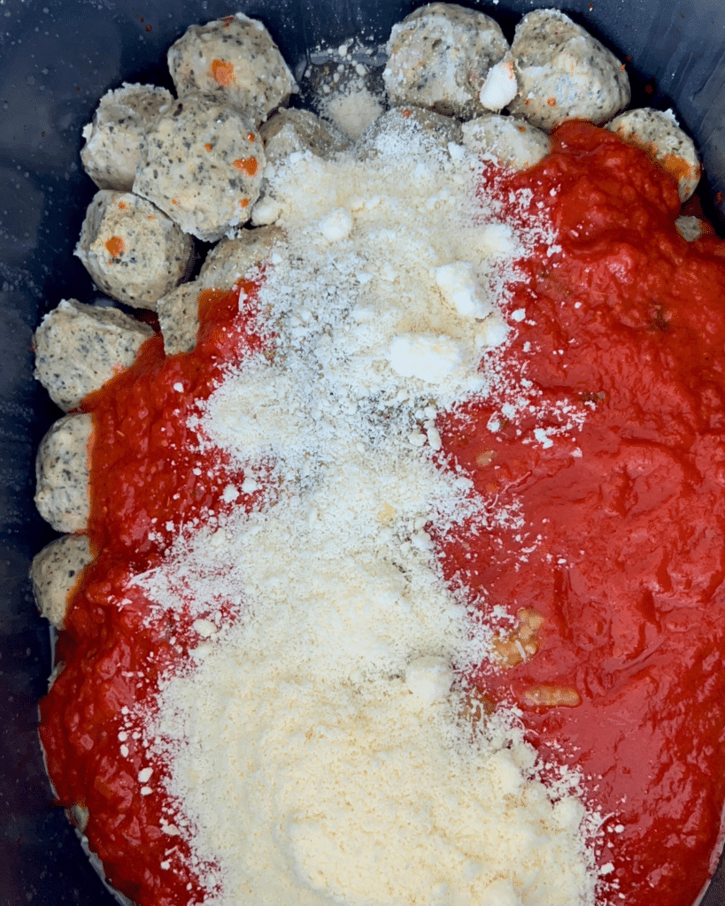 Meatballs in a slow cooker, partly covered with marinara sauce and topped with a sprinkle of Parmesan cheese.