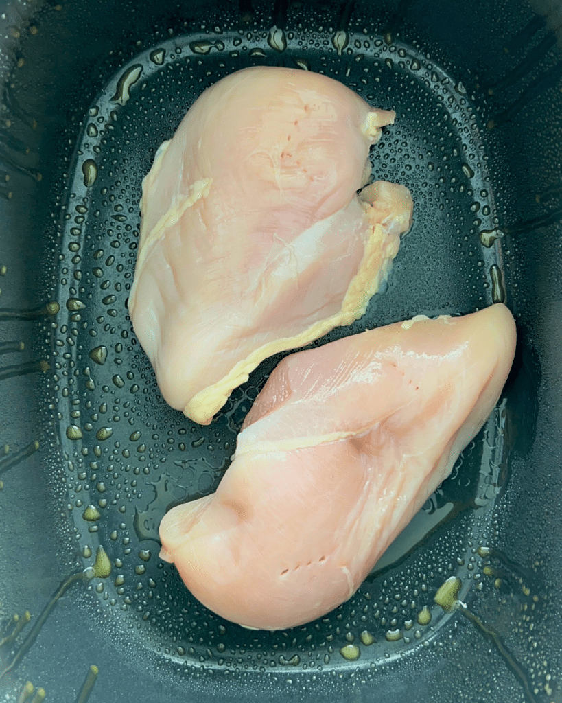 two chicken breasts in a greased black slow cooker