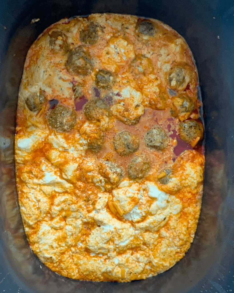 Meatballs covered in creamy orange sauce with melted cheese and tomato pieces, cooked together in a slow cooker.