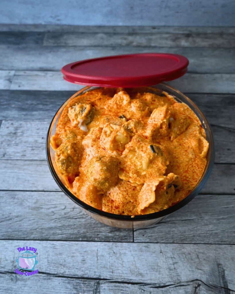 buffalo meatballs and tortellini in a glass storage bowl with a red lid