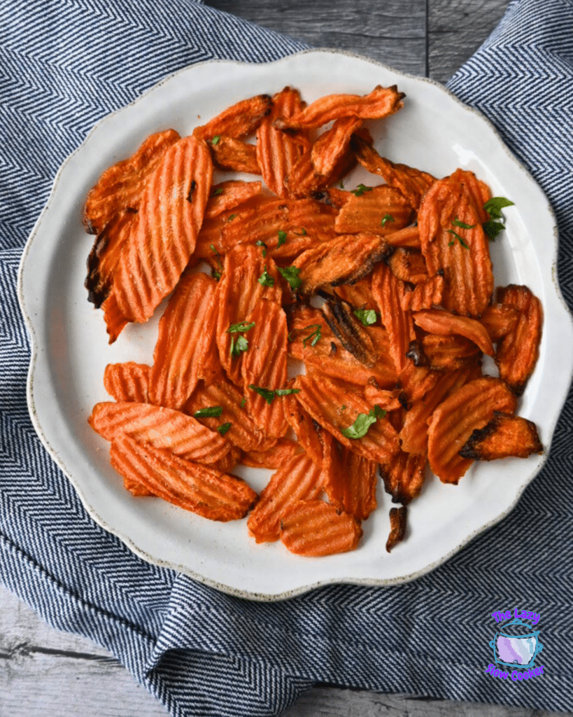 Crinkle-cut carrot chips topped with herbs are served on a white plate over a blue and white cloth.
