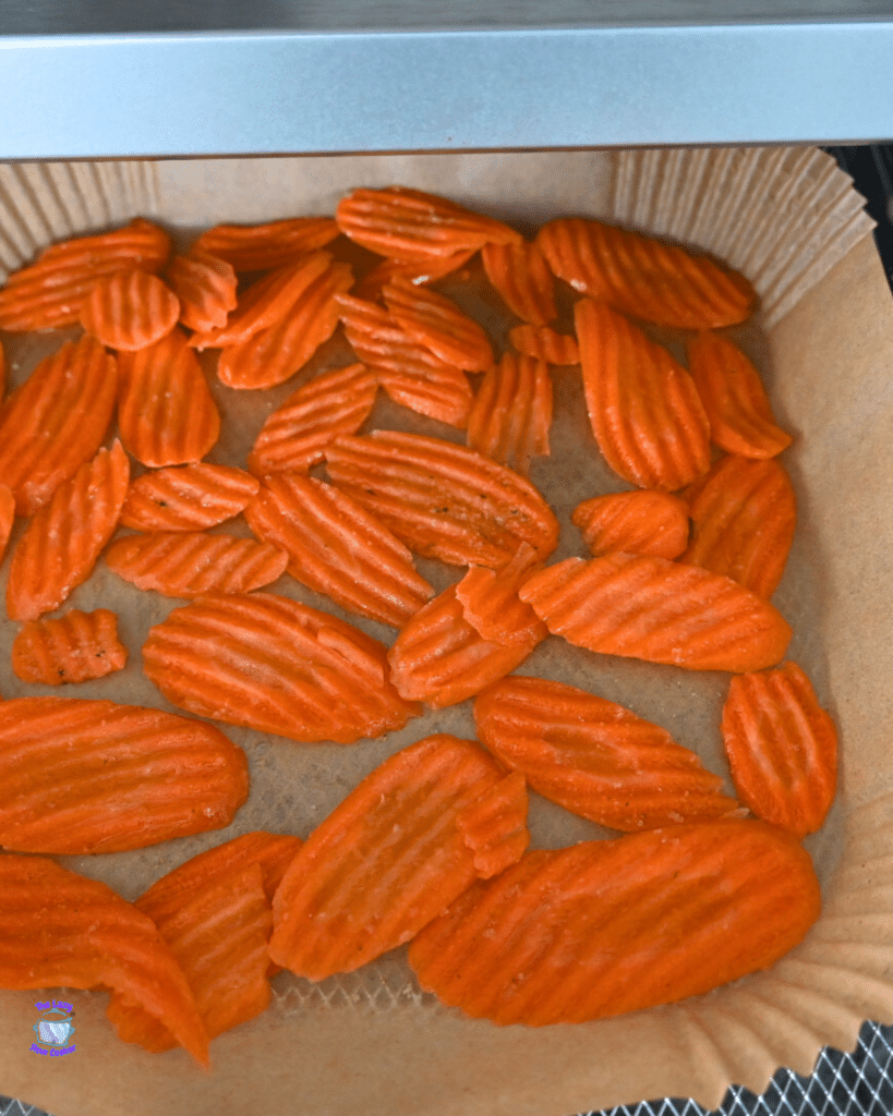 Crinkle-cut carrot chips are arranged in a single layer on parchment paper in a tray, ready to be air fried.