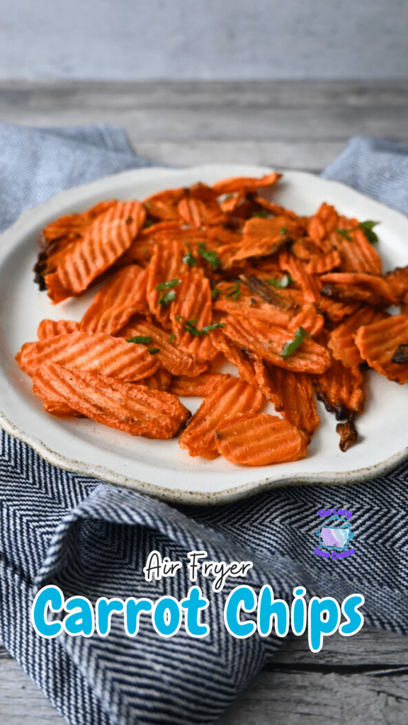 Crinkle-cut carrot chips topped with herbs are served on a white plate over a blue and white cloth.