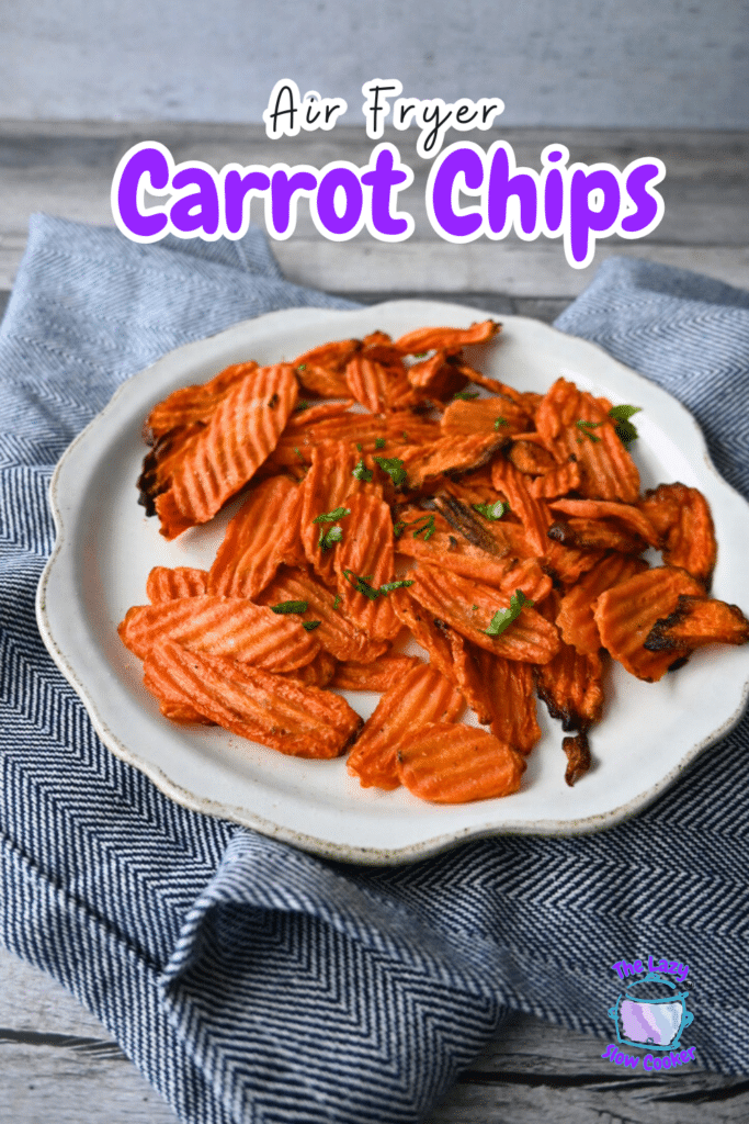 Crinkle-cut carrot chips topped with herbs are served on a white plate over a blue and white cloth. Text reads: Air Fryer Carrot Chips.