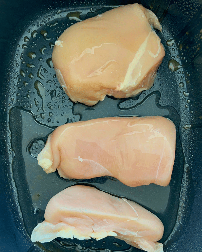three raw chicken breasts in a greased slow cooker