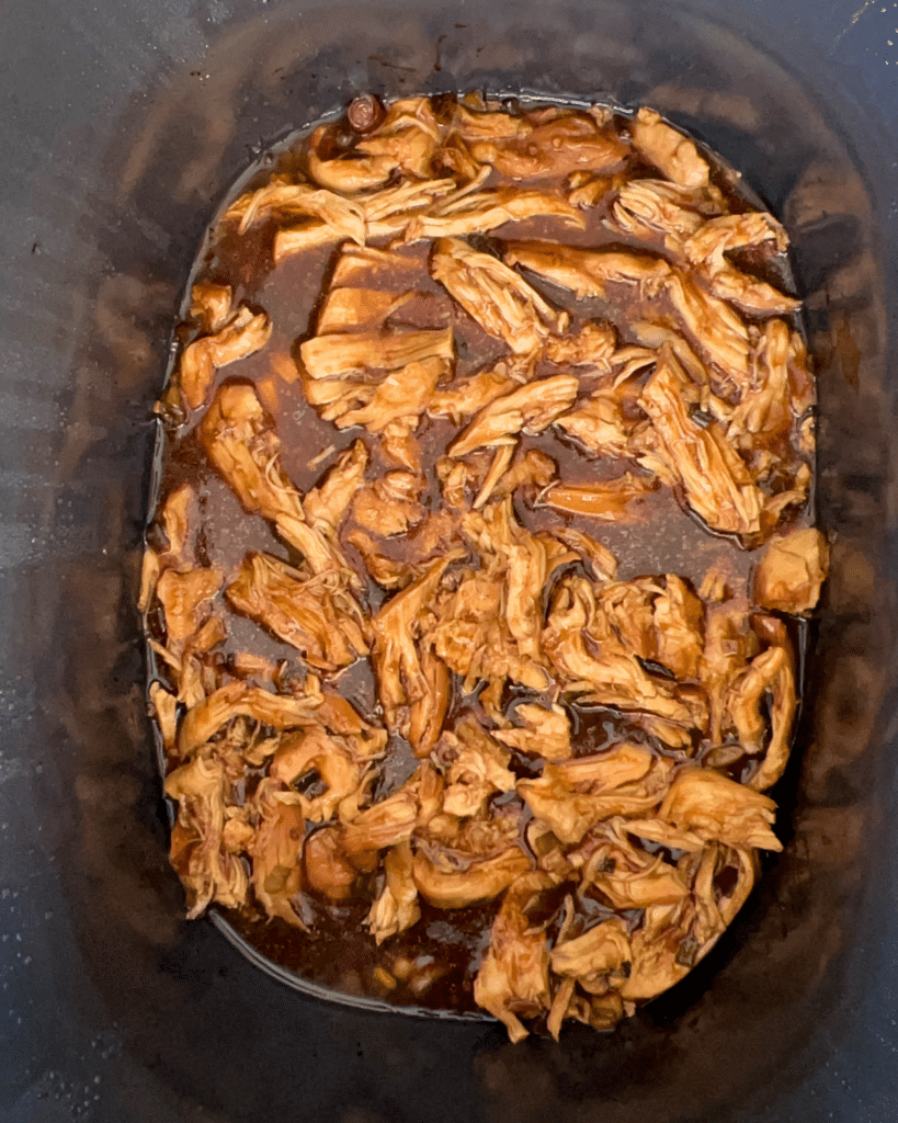 shredded cooked chicken in a savory brown sauce in a crockpot