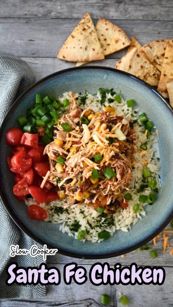 A bowl of slow cooker shredded chicken with corn, black beans, and rice, topped with cheese and green onions, served with tortilla chips.