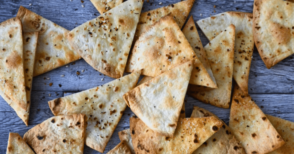 Golden-brown homemade air fryer pita chips, cut into triangles and seasoned, are spread out on a rustic wooden table.