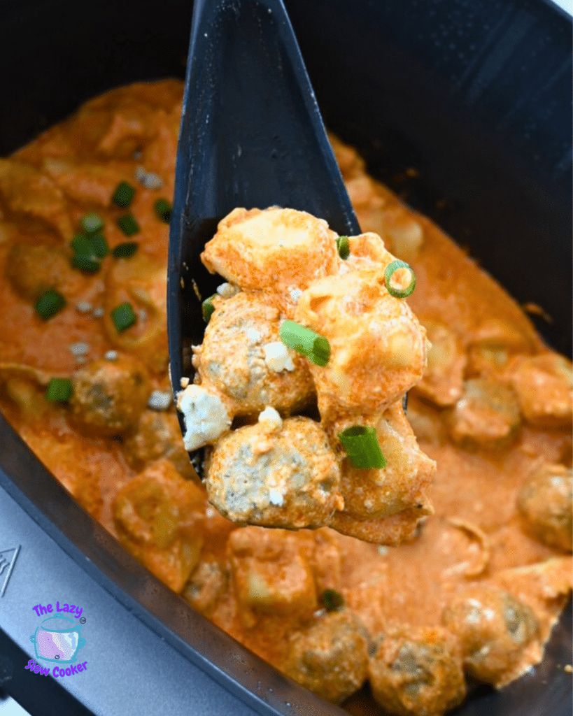 buffalo chicken meatballs and tortellini held on a large spoon over a slow cooker full of the same.