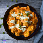 Buffalo chicken meatballs in orange sauce, topped with ranch and green onions, in a bowl on wood.