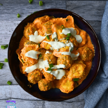 Buffalo chicken meatballs in orange sauce, topped with ranch and green onions, in a bowl on wood.