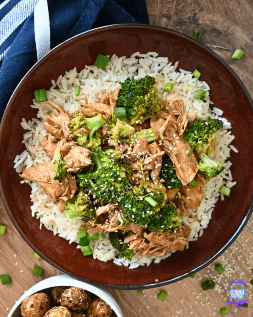 A bowl of white rice with shredded slow cooker chicken and broccoli, and sesame seeds