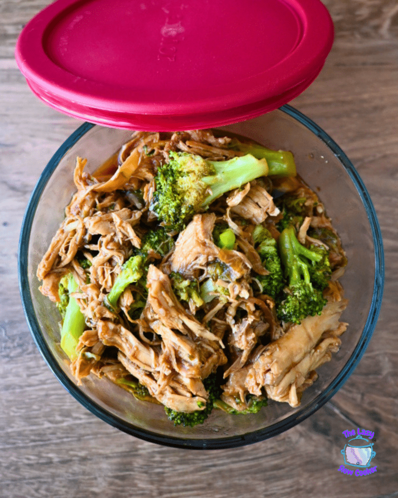 chicken and broccoli in a glass storage bowl with a red lid beside it.