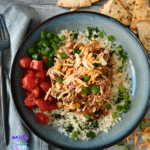 A bowl of slow cooker shredded chicken with corn, black beans, and rice, topped with cheese and green onions, served with tortilla chips.