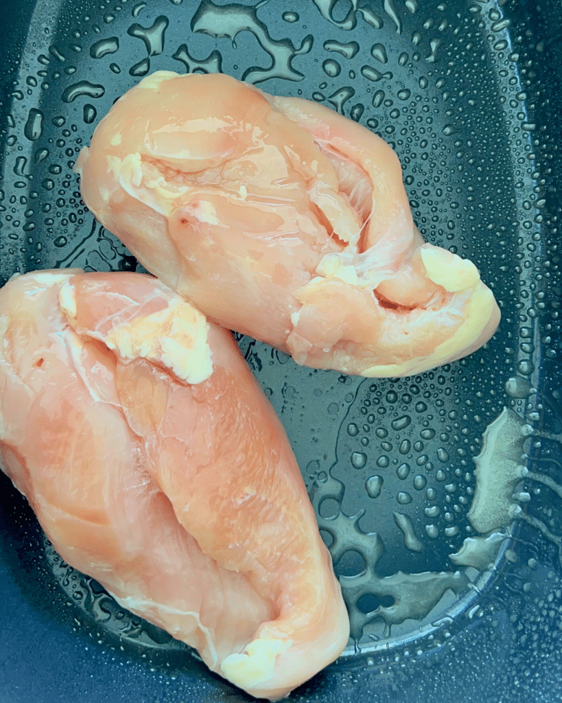 two raw chicken breasts in a greased slow cooker