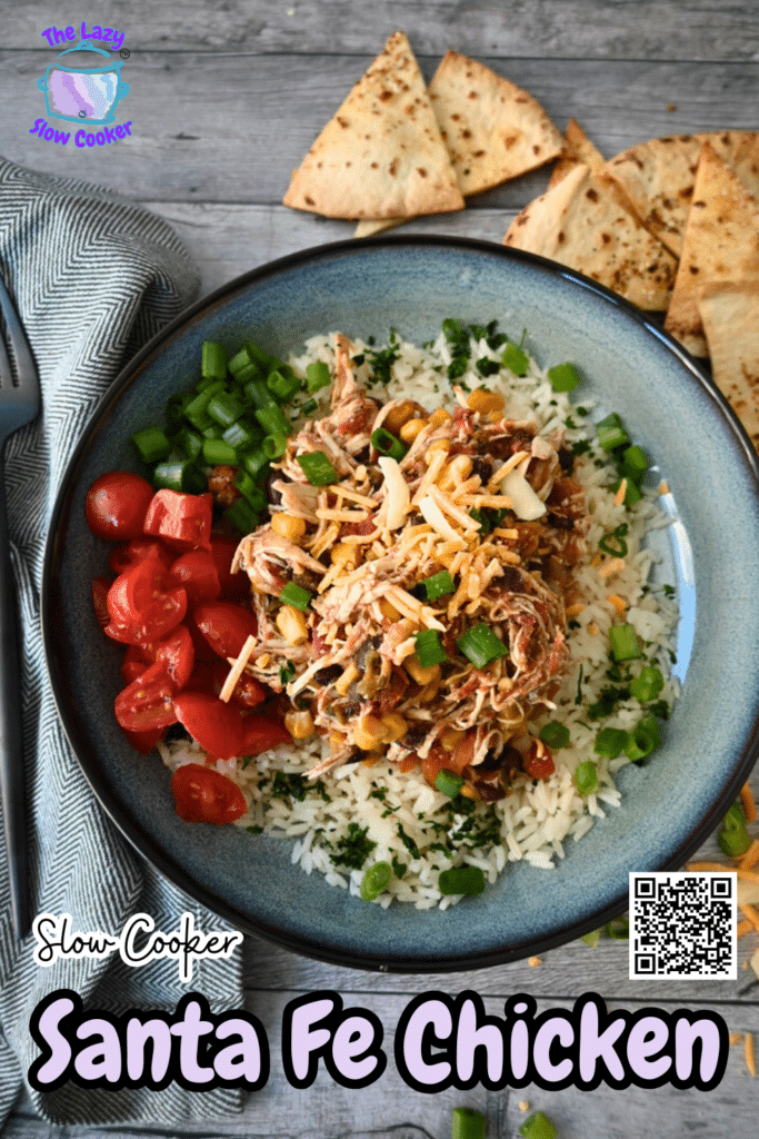 A bowl of slow cooker shredded chicken with corn, black beans, and rice, topped with cheese and green onions, served with tortilla chips.