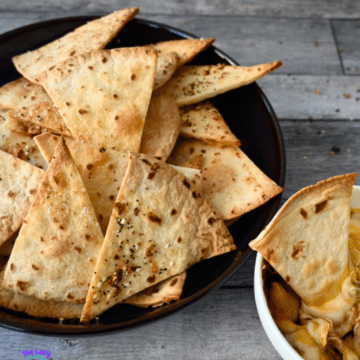 Crispy air fried tortilla chips in a black bowl on a wooden table with a gray cloth.