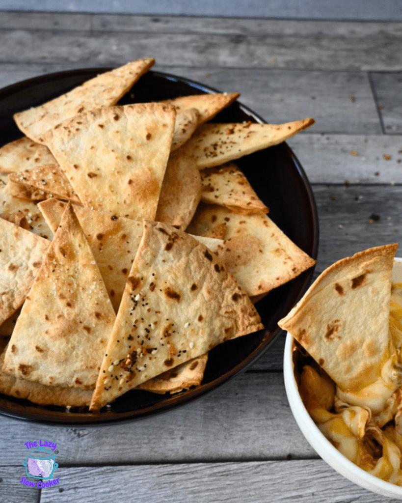 Crispy air fried tortilla chips in a black bowl on a wooden table with a gray cloth.