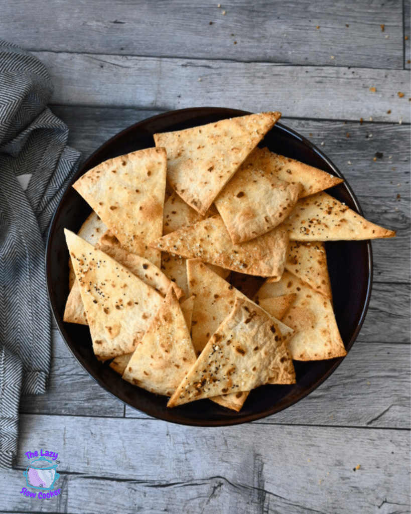 Crispy air fried tortilla chips in a black bowl on a wooden table with a gray cloth.