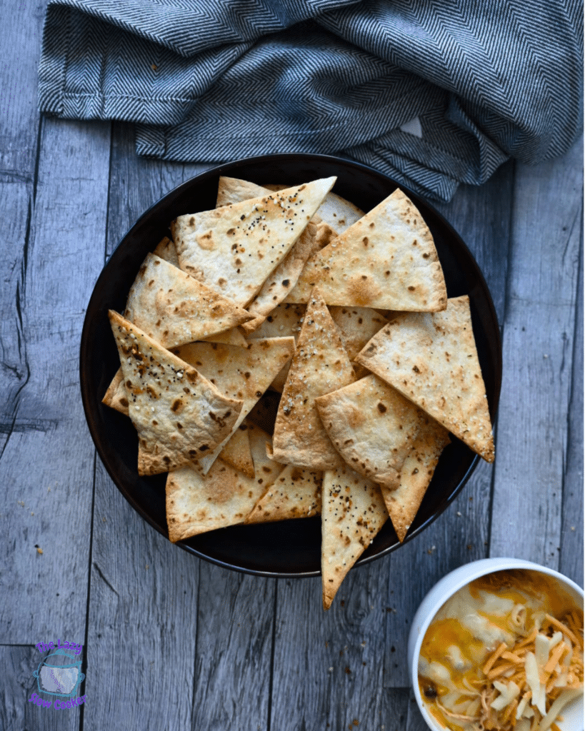 Crispy air fried tortilla chips in a black bowl on a wooden table with a gray cloth.
