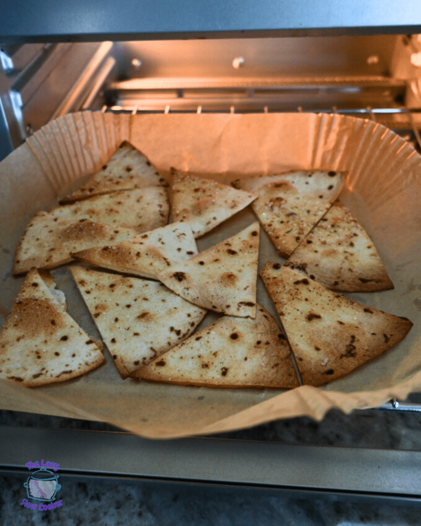 A tray of homemade tortilla chips in an oven style air fryer turning golden brown and coated with seasoning.