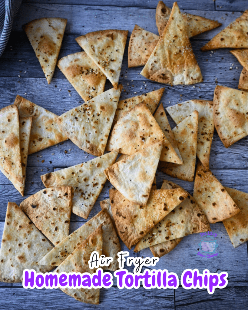 Golden-brown homemade air fryer pita chips, cut into triangles and seasoned, are spread out on a rustic wooden table.